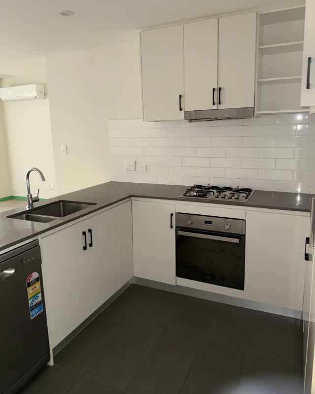 The same apartment's kitchen at handover, with the oven front, gas cooktop, rangehood, tiled splashback, benchtops and floor all cleaned down