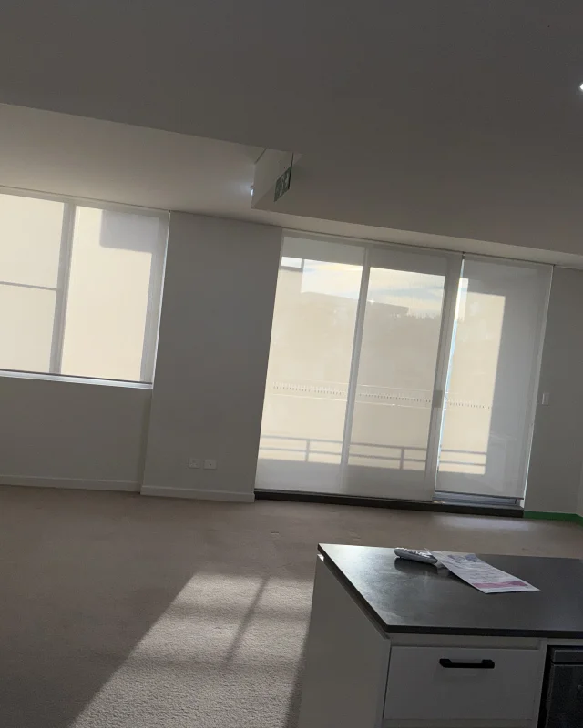 Vacated apartment living and dining area at handover, carpet vacuumed, balcony door glass and blinds clean and the benchtop cleared