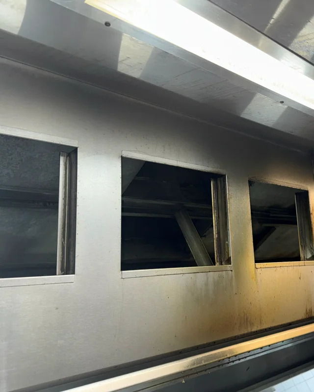 Grease-stained interior of a commercial kitchen exhaust canopy before degreasing, filter slots removed