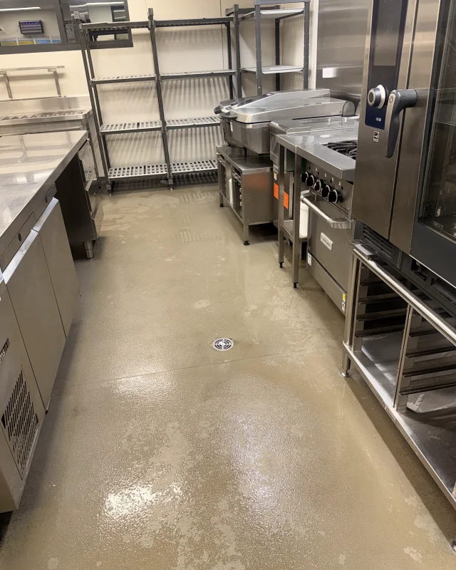 Commercial kitchen cooking line after deep cleaning, the floor, drain, wire shelving and stainless equipment cleaned down