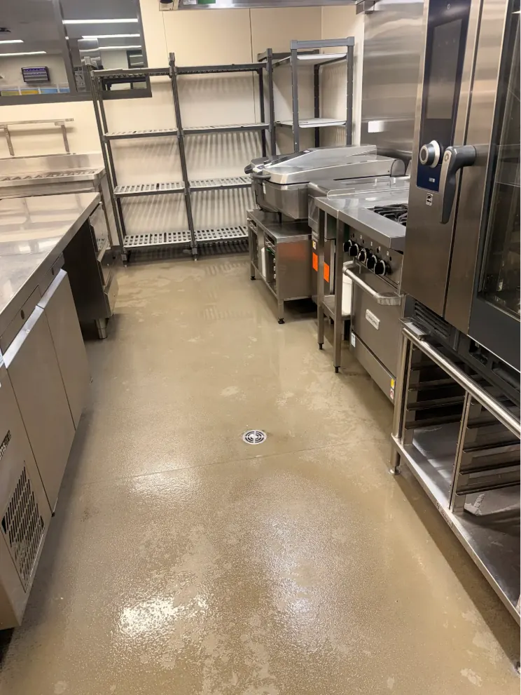 Commercial kitchen after a deep clean, with freshly mopped floor, shelving and cooking equipment