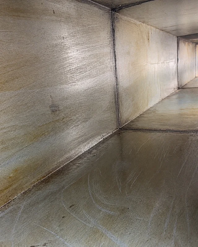 The same duct run after cleaning, the walls and base scoured back to bare metal with the grease deposit gone