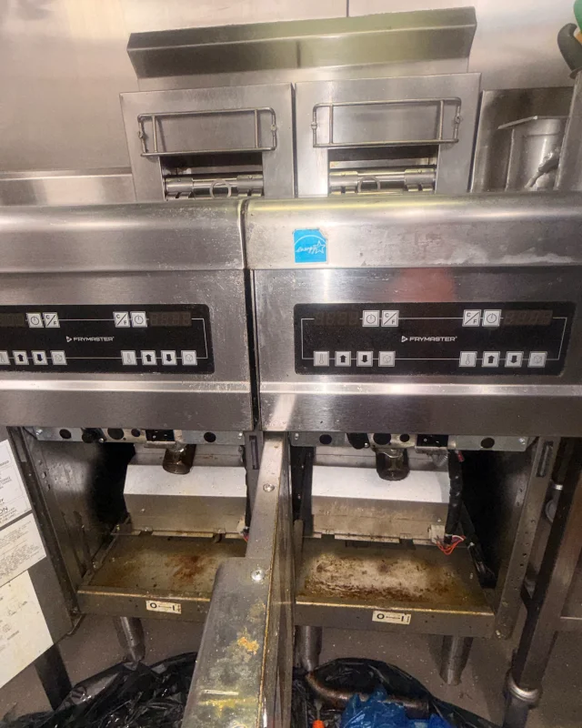 Two commercial fryers with grease-stained control panels, surrounds and open cabinet floors before degreasing