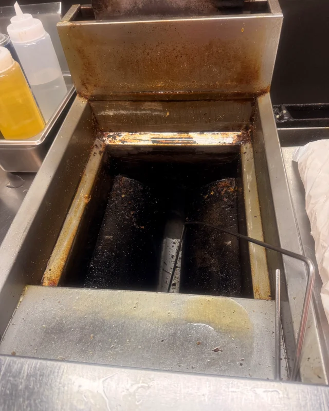 Fryer heating elements crusted with burnt carbon under a grease-caked splash guard before cleaning
