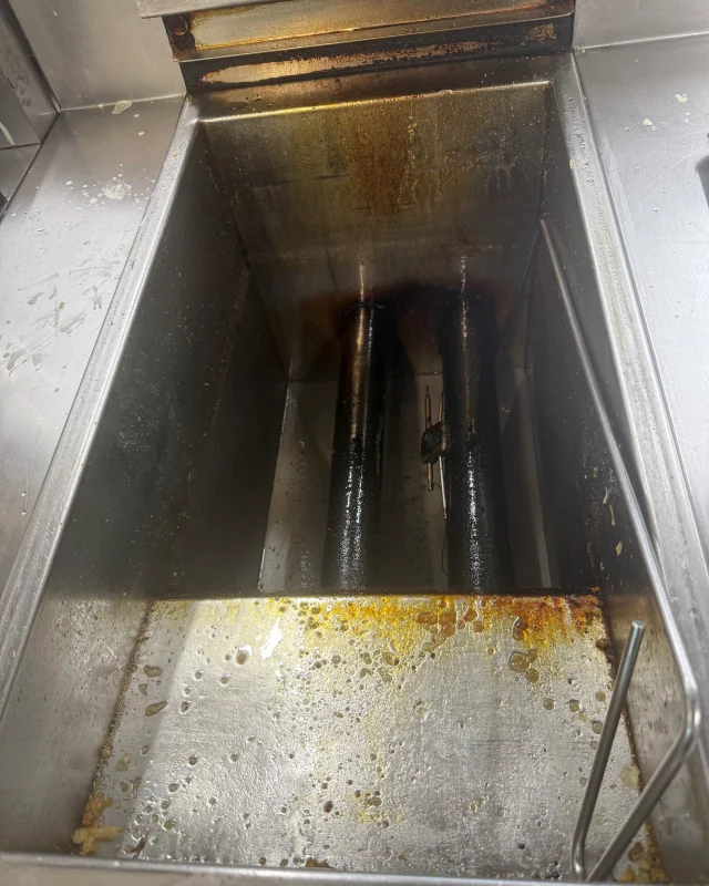 Commercial deep fryer vat with burnt-on oil across the base and carbonised heating elements before a boil-out