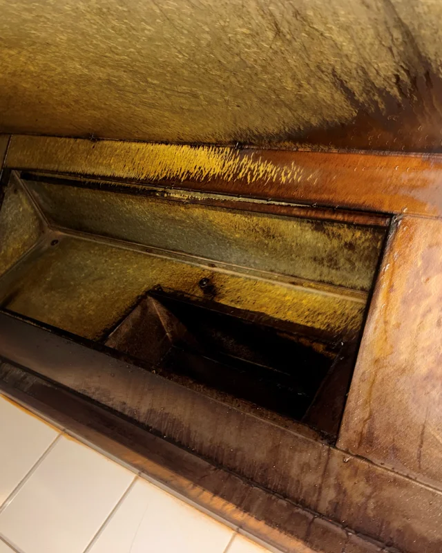 Hardened grease coating the capture edge, gutter and duct collar of a commercial kitchen canopy before cleaning