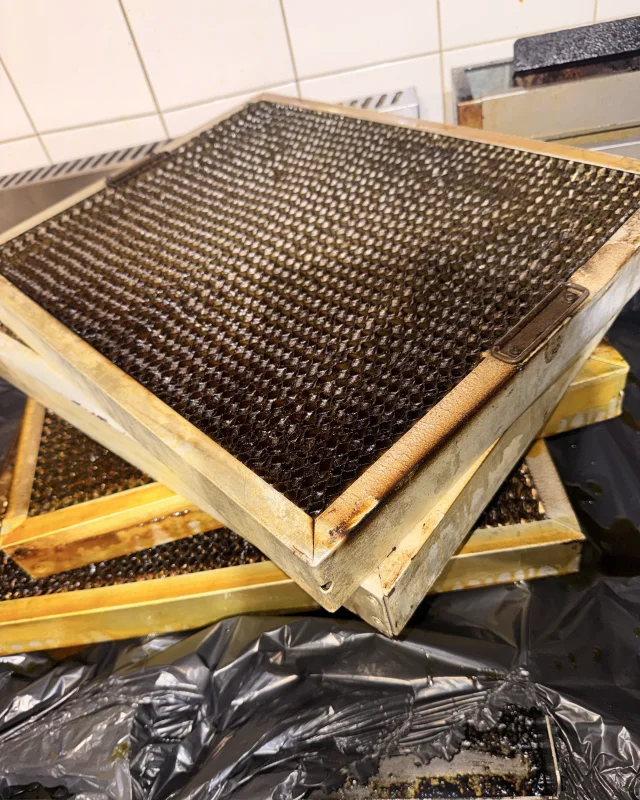 Commercial kitchen canopy mesh filters caked in hardened black grease before cleaning
