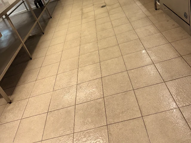 Commercial kitchen tiled floor at the end of a wash down, water still standing across the tile faces beside a stainless bench