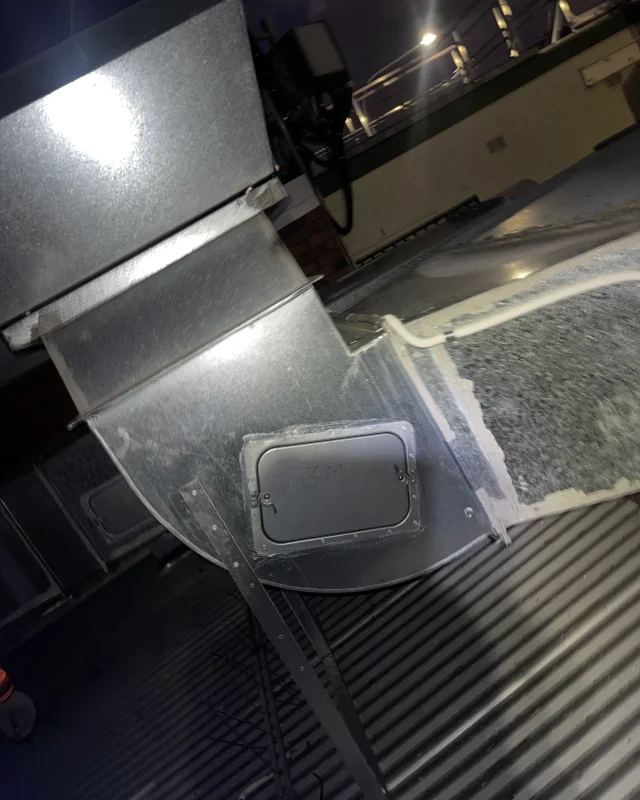 The same rooftop ductwork after an access panel was cut into the elbow and fitted, its frame sealed against the duct