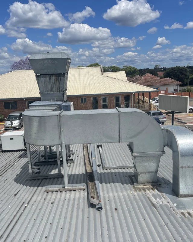 Rooftop commercial kitchen exhaust duct run with a sealed face and no access point, its fan cowl above and the elbow turning down to the roof sheet