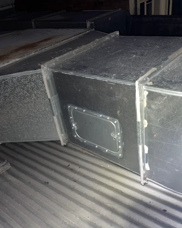 A hinged access panel fitted into the same rooftop ductwork and sealed around its frame, photographed on the night of the install