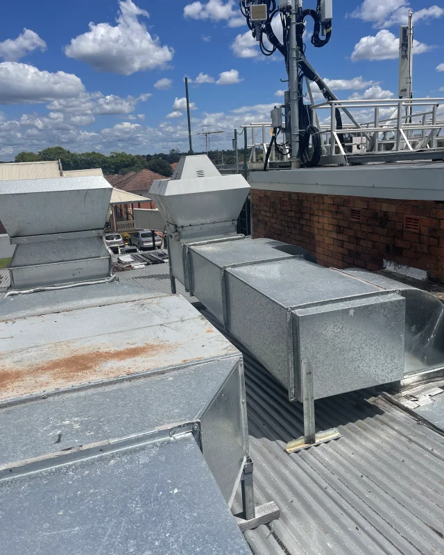 Rooftop commercial kitchen exhaust ducting running to a brick wall, sealed along its length with no access point
