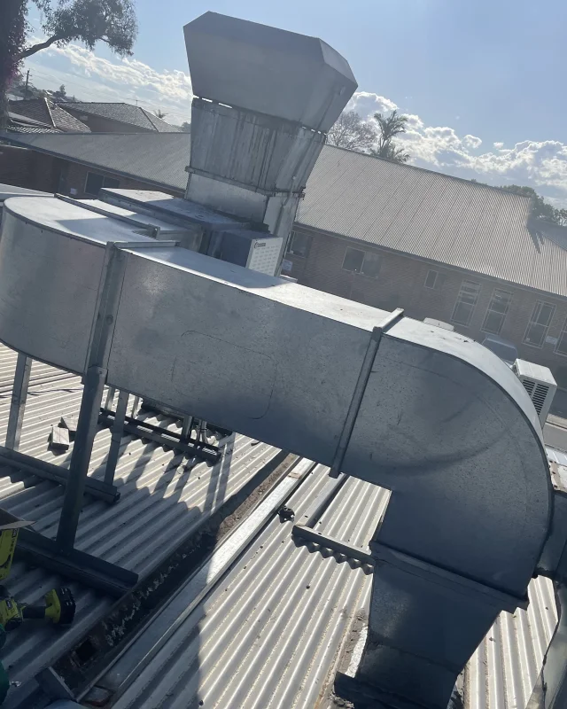 A rooftop commercial kitchen exhaust run with an access panel position pencilled onto the duct face and cutting tools on the roof beside it