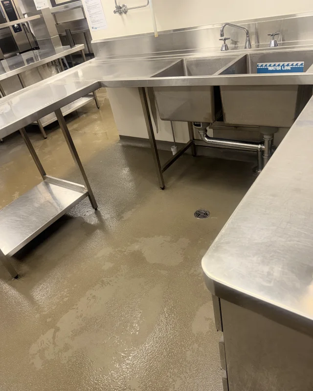 Commercial kitchen wash-up bay after deep cleaning, the floor, sink and benches back to bare stainless and sealed concrete